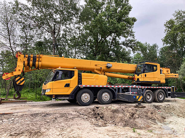 istock Yellow construction crane on a dirt area with sparse vegetation, overcast sky, trees in the distance, soft shadows, lattice boom structure, multiple axles, enclosed cab, heavy machinery 2233683277