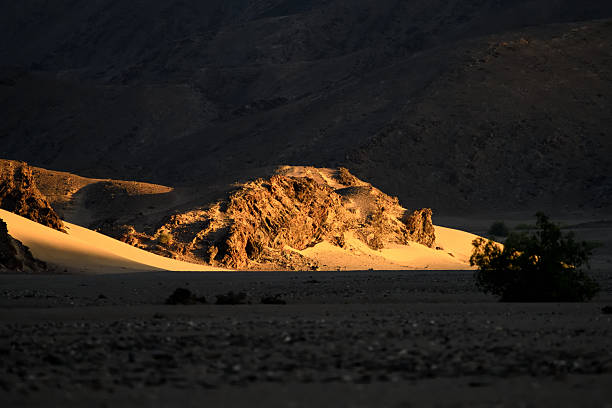 The setting sun highlight a small hill in the Hoanib Valley, illuminating the sand dunes collecting at the base of the hill