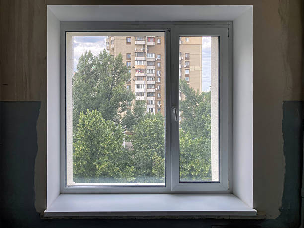 istock Room with two windows, one closed and one open Light-colored walls and flooring, tree tops visible outside both windows against a clear sky Multi-story building in the background with balconies and 2233683402
