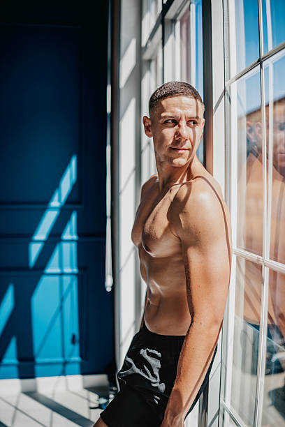 istock Fit athletic man flexes muscles while standing by a window in bright indoor setting 2233684573
