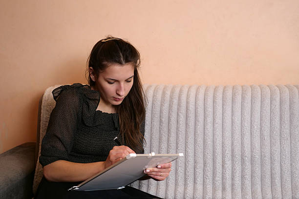 istock A girl draws with a marker on a board while lying on a sofa. 2233684676