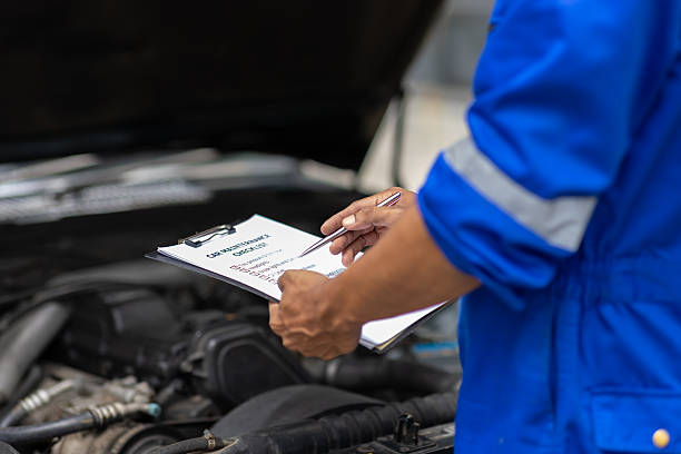 istock Car mechanic inspecting engine and taking notes on clipboard. Mechanic in a uniform is holding a clipboard and inspecting a car engine, taking notes while assessing the vehicle's condition. 2233684698