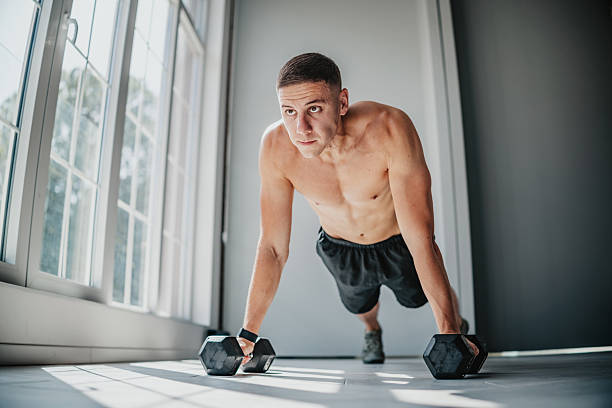 istock Fit man performs push-ups with dumbbells in an indoor gym setting focusing on strength training and fitness 2233685316