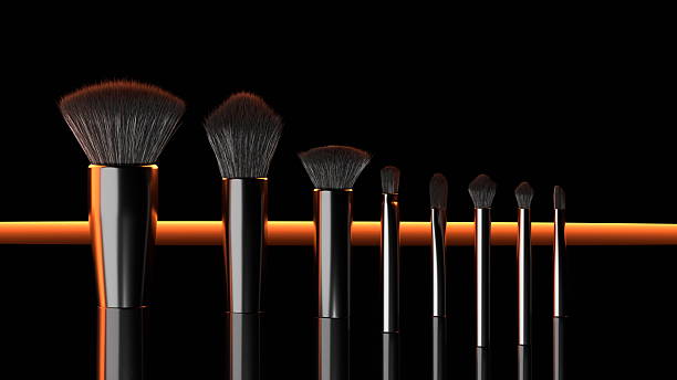 Makeup brushes of different sizes are neatly lined up on a reflective surface with a striking black backdrop and vibrant orange lighting, creating a modern look