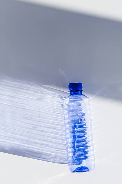 Blue plastic water bottles on white blue background with sunlight shadow and sun flare, Minimal top view photo, themes of ecology, recycling, sustainable living, reduce disposable plastics