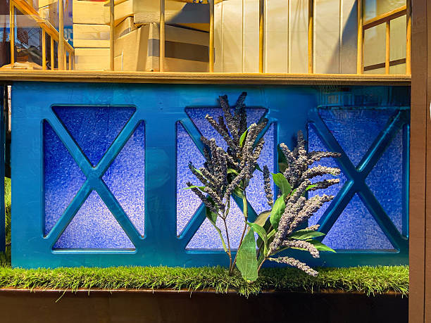 Contemporary art display features a blue wall divided into nine abstract panels, each with unique texture and color A lush plant in a planter adds natural contrast Two wooden slats lean against the