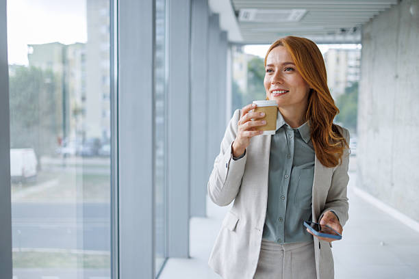 istock Businesswoman drinking coffee and using smartphone in office corridor 2233690726