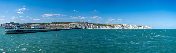 This image captures the iconic White Cliffs of Dover with the harbor in the foreground, under a bright summer sky. The chalk cliffs contrast with the deep blue sea and the industrial port structures. A symbol of British resilience and natural beauty, ideal for themes of travel, heritage, and coastal landscapes.