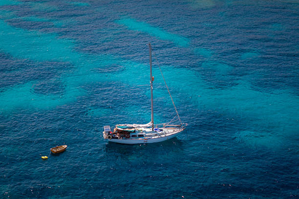 A sailboat anchored in crystal-clear turquoise waters of the Mediterranean Sea. The vibrant shades of blue create a peaceful and scenic maritime view, perfect for leisure and travel imagery.