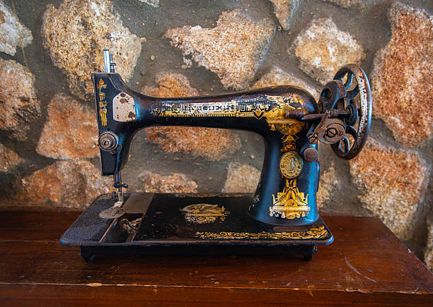 Setenil de las Bodegas, Spain - March 11, 2025: Antique black sewing machine with gold detail placed on wood surface. Rustic decor at local restaurant with stone wall backdrop.