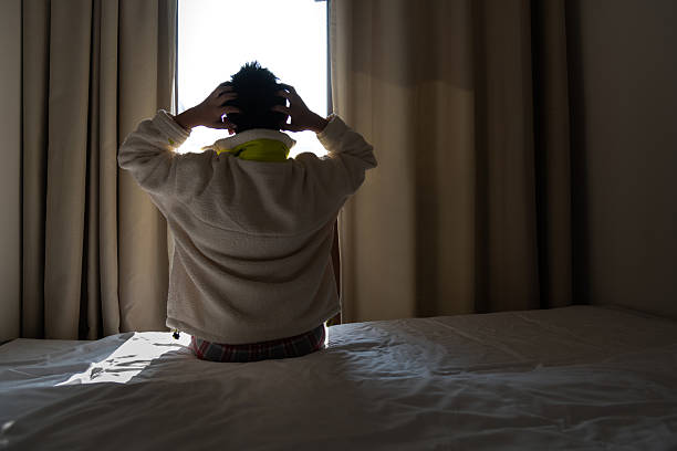 Depressed teenager boy sitting on bed with head in hands