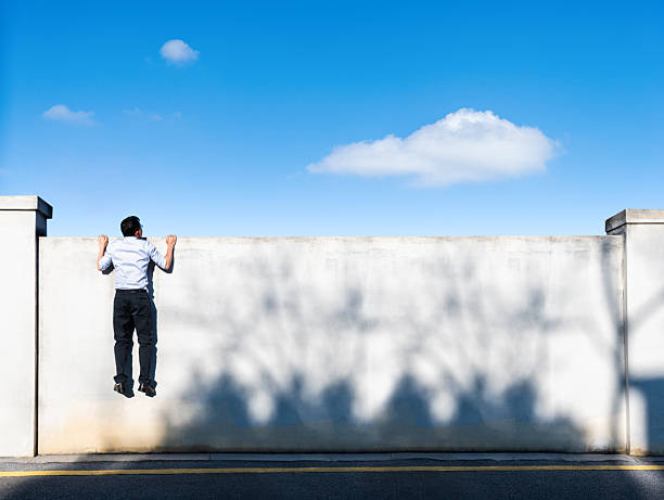 istock Young businessman climbing over a concrete wall with blue sky background 2233706429