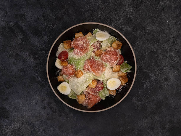 Enjoy a colorful Caesar salad with salmon,lettuce leaves, quail eggs, fresh veggies, cherry, and crispy toppings for added texture and flavor on black background.