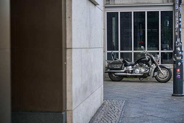 Motorcycle parked beside modern building in Berlin, architecture focus, daylight, clean urban feel, horizontal orientation, ideal for automotive, urban lifestyle, architecture, and commercial usages.