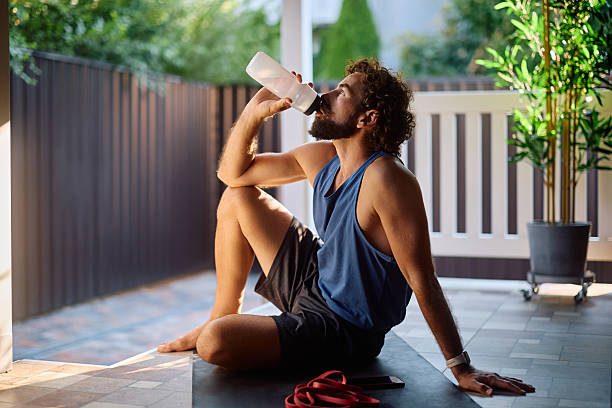istock Athletic man drinking water from a bottle while exercising on patio at home. 2233714735