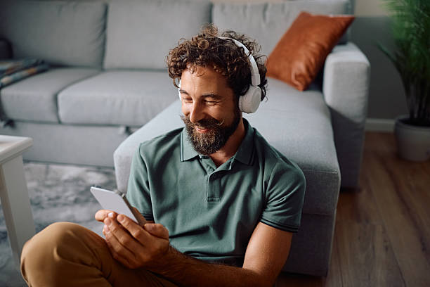 istock Happy man using cell phone while listening music over headphones at home. 2233715531