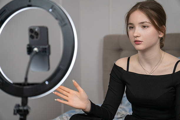 istock Young influencer sitting on bed, recording video blog using smartphone and ring light, creating engaging content for online audience in her bedroom 2233724045