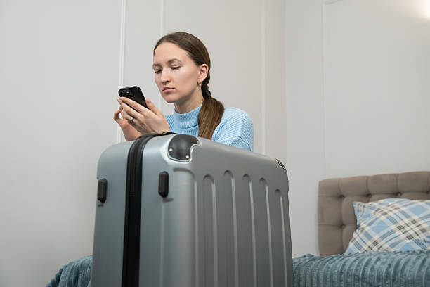 istock Young woman sitting on a hotel bed, surrounded by a packed suitcase, using a smartphone to finalize travel plans, preparing for departure or arrival during her journey 2233727086