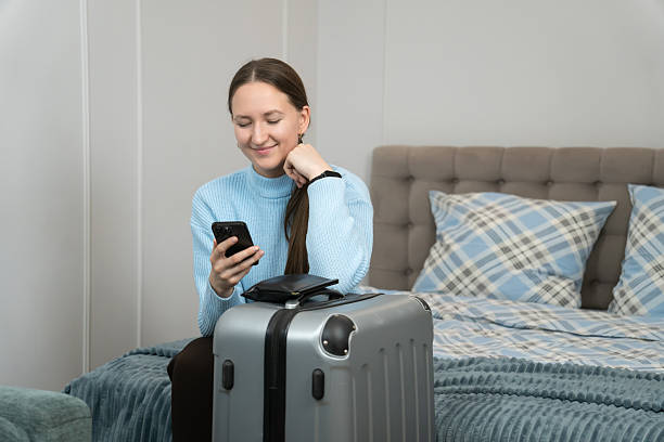 istock Young woman sitting on a bed next to a packed suitcase, using her smartphone to finalize travel plans for an upcoming business trip or vacation, embracing modern technology for convenience 2233727201
