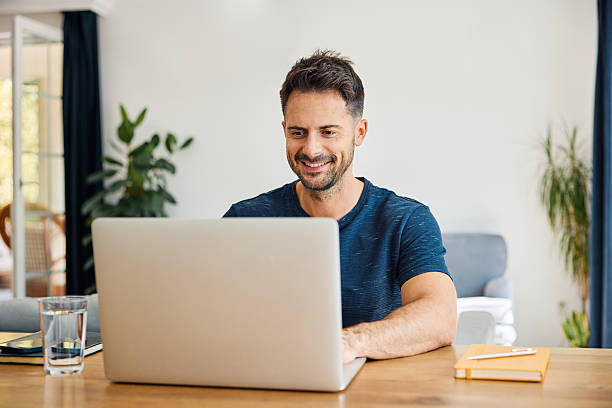 istock Smiling man sitting at desk with laptop at home 2233736322