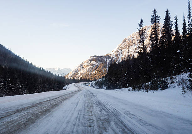 istock Snowy Road Through Pine Forest and Mountain Landscape at Sunrise 2233740715
