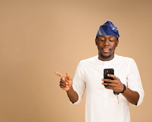 istock Man in traditional attire smiling while pointing and holding phone 2233745903