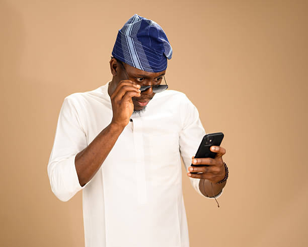 istock Man in traditional attire adjusting sunglasses while looking at phone 2233746192