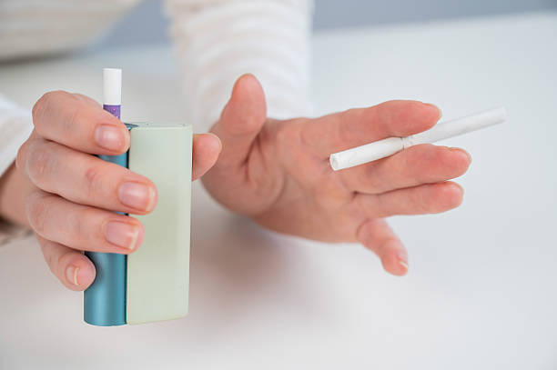 istock Woman holding regular and electronic cigarette on white background. Tobacco heating systems. 2233747825