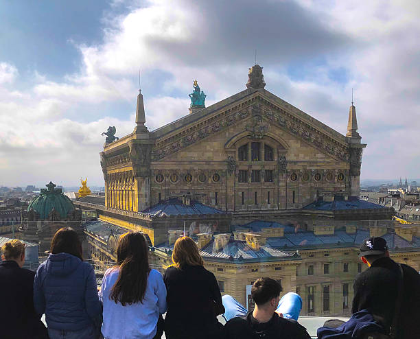 Paris, France - March 28, 2025: Tourists sitting looking over rooftops and the Opera Garnier.