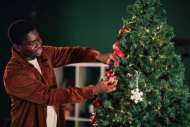 istock Young man decorating christmas tree with red balls and lights 2233749849