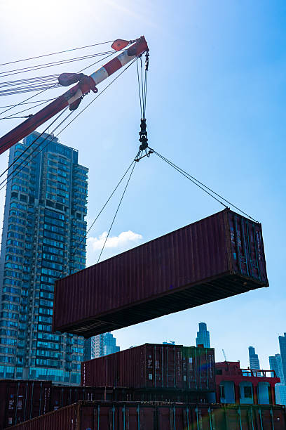 Crane lifting a cargo container in a busy port area with skyscrapers in the background