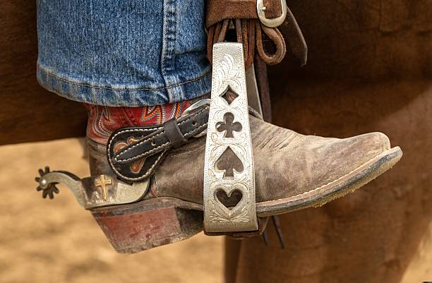 A closeup view of a custom designed silver stirrup with a colorful leather western style boot and a spur.