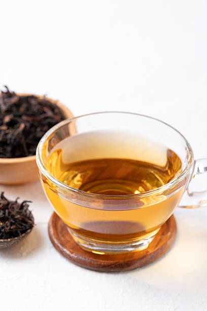 Black tea in cup glass with dried tea leaves on white background