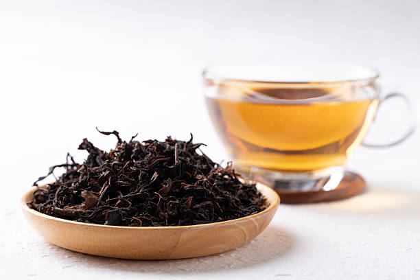 Dried black tea leaves and hot tea in cup glass on white background Dried black tea leaves in wooden bowl and hot tea in cup glass on white background, Healthy herbal drink tea supplement stock pictures, royalty-free photos & images