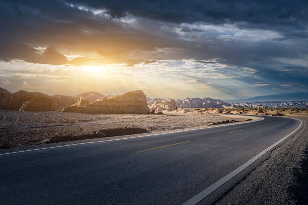 istock Winding asphalt highway curves through dramatic desert landscape with yardang landforms under a beautiful sunset 2233760548