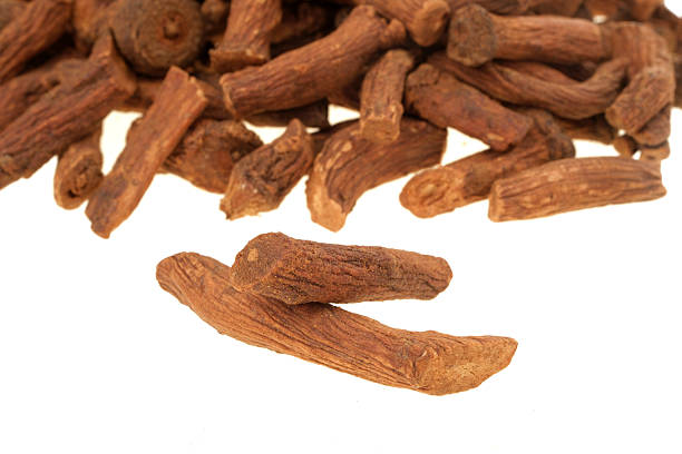 A close-up image of pieces of dry galangal root resting on a wooden bedside table. One piece appears partially burnt, symbolising its use in natural, alternative medicine. This detail reinforces the connection to holistic, new age practices.