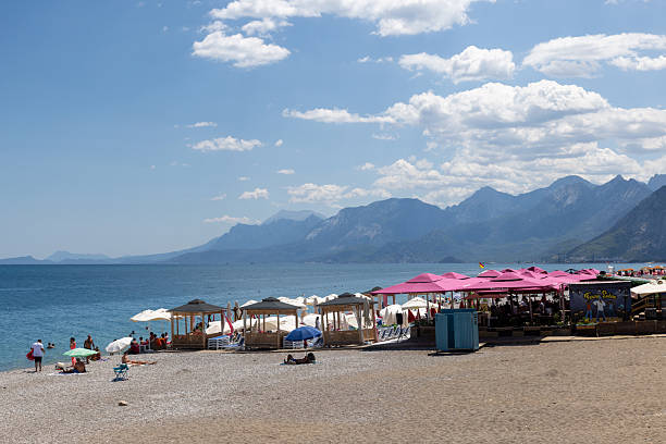 Antalya, Turkey - July 9, 2023: The beach stretches for 7 km from the cliffs to the Beydaglari mountains. A lot people area enjoy on the beach.