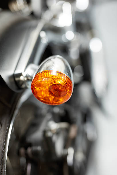 Detail view of an orange motorcycle signal light with a blurred metallic body background. The image highlights design and engineering in automotive parts, emphasizing sophistication and functionality.