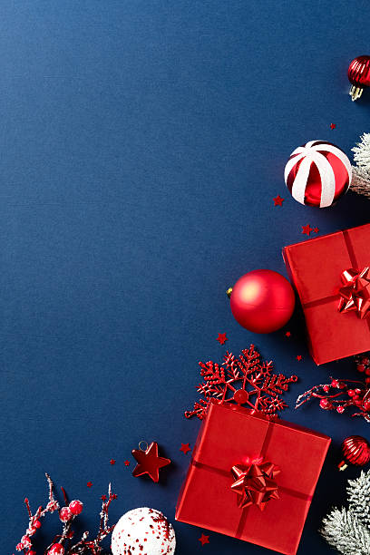 istock Elegant Christmas flat lay composition with red gift boxes, baubles, snowflakes, berries, and frosted pine branches on dark blue background 2233784743