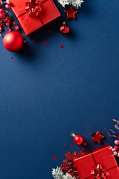 istock Stylish Christmas frame with red gift boxes, baubles, berries, frosted pine branches, and star confetti on dark blue background. Center space for text, 2233784803
