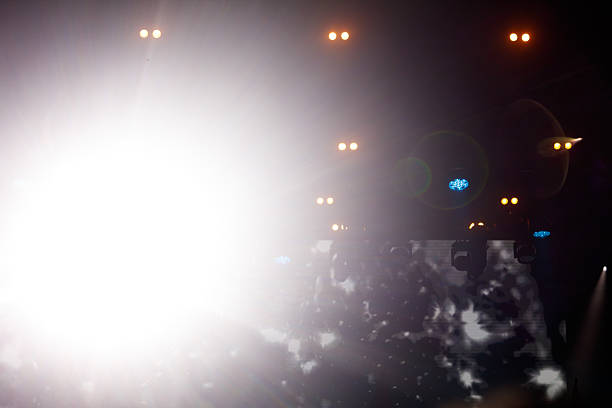 A bright light shines through the darkness, illuminating the scene. The light is coming from a car's headlights, which are on in the dark. The scene is a busy highway, with many cars