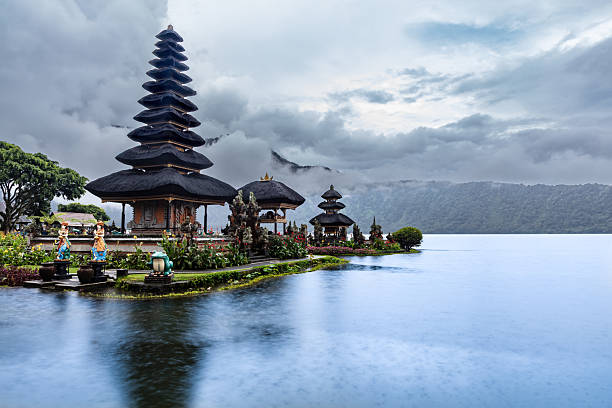 Pura Ulun Danu Bratan (Temple by the Lake) Hindu Shaivite temple on the shores of Lake Bratan, in the mountains of Bali, Indonesia. Clouds and mountains in background. Calm lake surrounds the site.