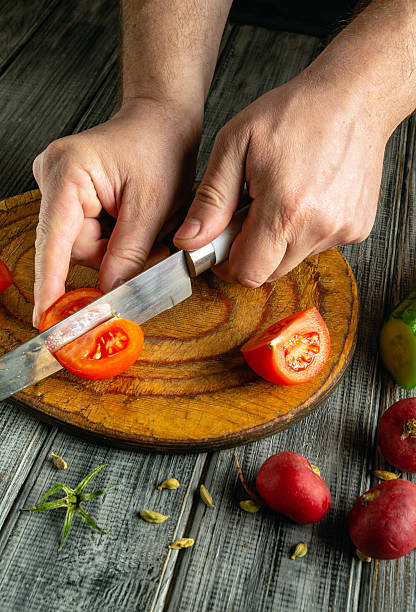 istock Hands skillfully cut ripe tomatoes on a rustic wooden cutting board. Surrounding the board are various fresh vegetables, enhancing the cooking atmosphere in a cozy kitchen 2233792881