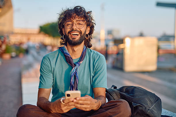 istock Stylish young man laughing while using smartphone outdoors 2233801477