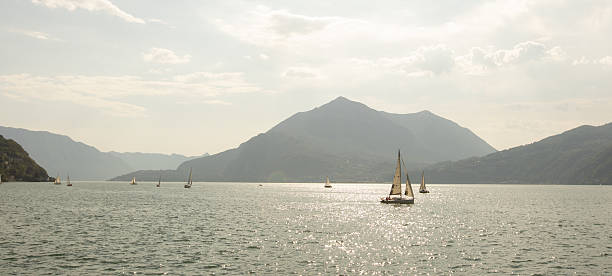 Small sailboats navigate the calm waters of the lake, surrounded by lush hills and the beauty of nature on a warm afternoon.