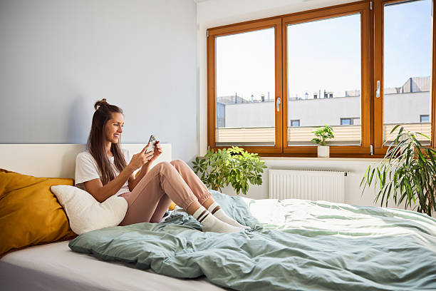 istock Smiling woman sitting on bed using her phone in a sunny apartment. 2233803049