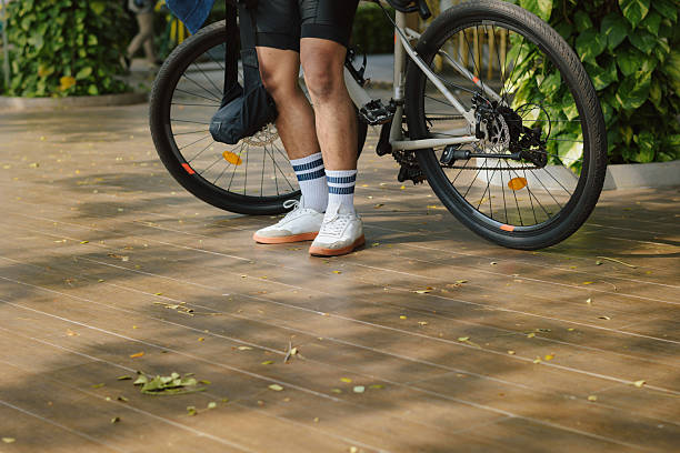 Close-up, rear view of Asian man in sportswear stops and rests beside his bike in the city park during morning ride. Outdoor activity, relaxation, and healthy routine