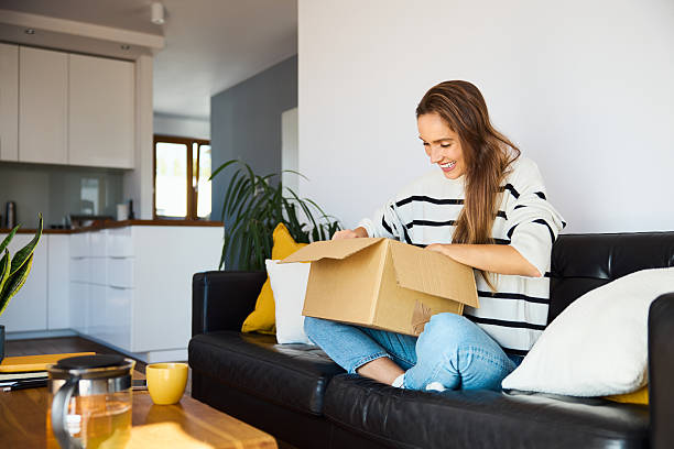 istock Woman unboxing e-commerce delivery package sitting on sofa in her apartment 2233809960