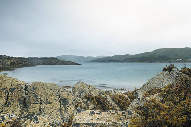 Long exposure view of the Arisaig coastline in the Scottish Highlands, with smooth waters, cloudy skies, and rocky foreground.