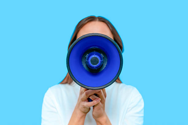 istock Woman holds a blue megaphone to her mouth against a solid blue background while expressing excitement and enthusiasm for a lively gathering 2233817809